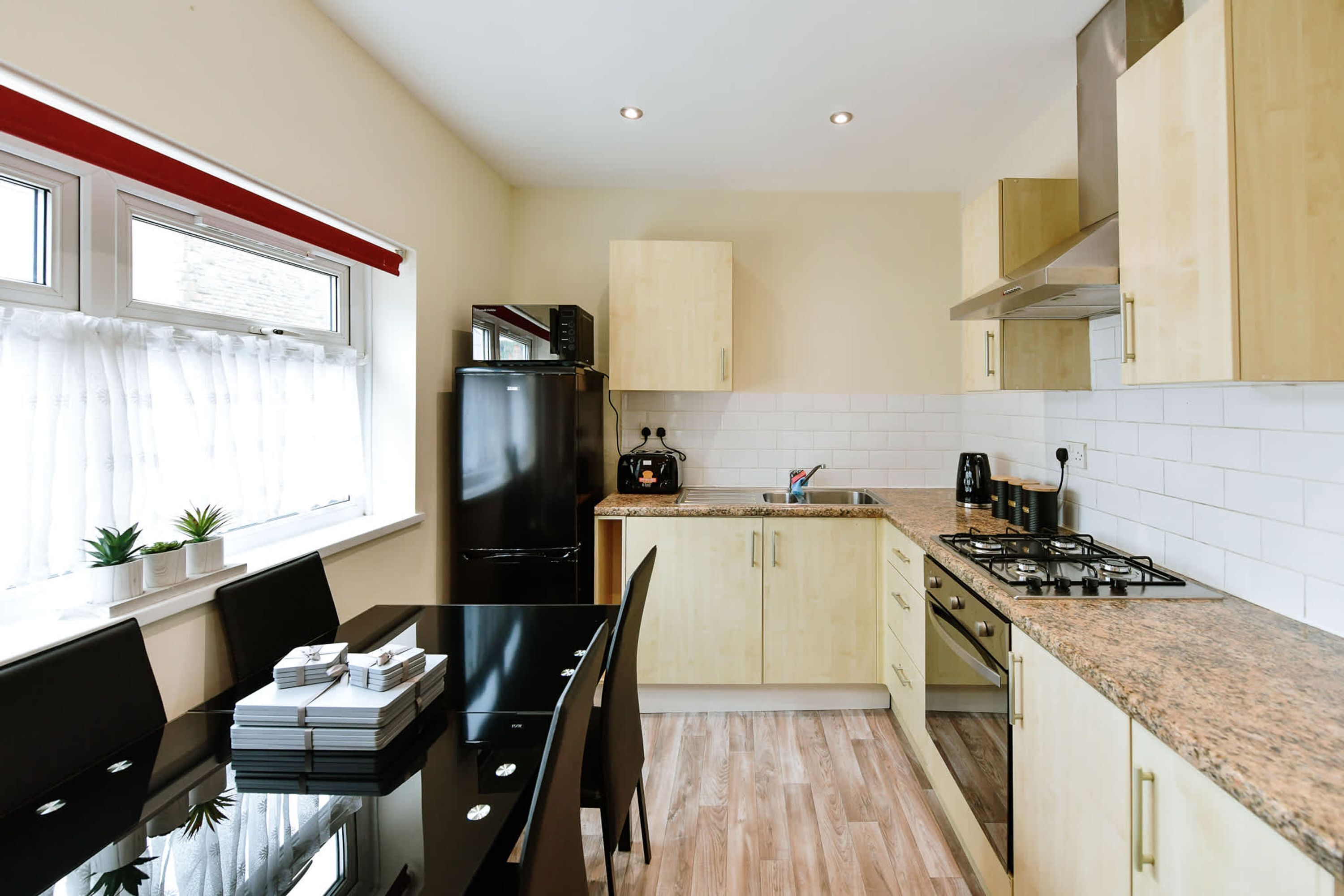 A modern kitchen with a dining area, featuring a black refrigerator, a stove, and wooden cabinets.