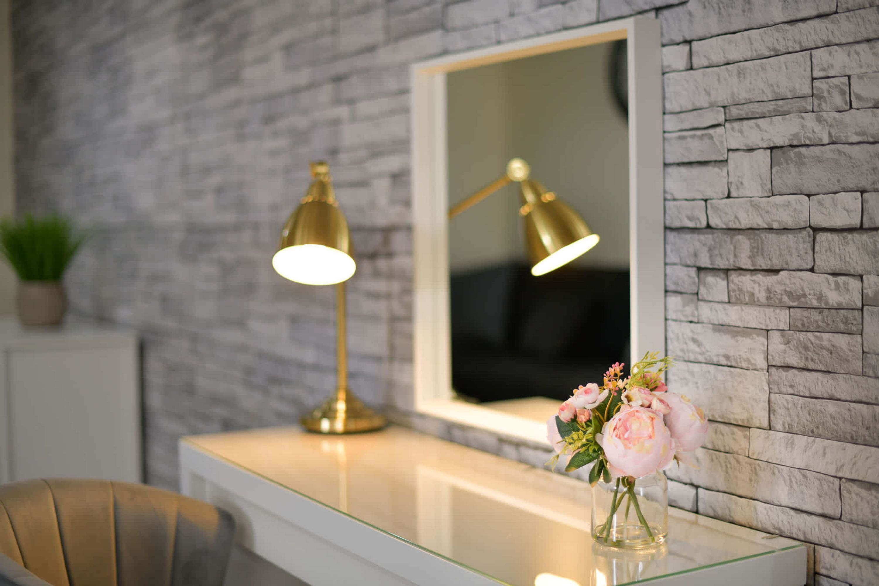 A modern room with a glass desk, a gold lamp, and a vase of flowers.