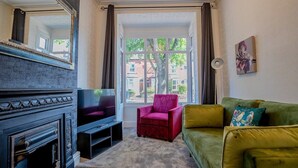 A living room with a fireplace, a television, a green sofa, and a red armchair. - Host Stay Somerset Road House (Birmingham)