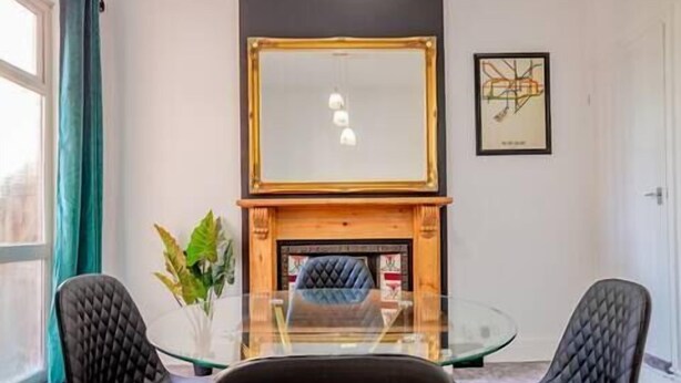 A room with a glass table, two black chairs, a fireplace, and a framed picture on the wall. - Host Stay Somerset Road House (Birmingham)