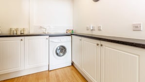 A compact kitchen with a built-in washing machine, white cabinetry, and a clock on the wall. - Host Stay Club Chambers (Malvern)