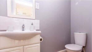 A bathroom with a white sink, mirror, and toilet against a light purple wall. - Host Stay Club Chambers (Malvern)