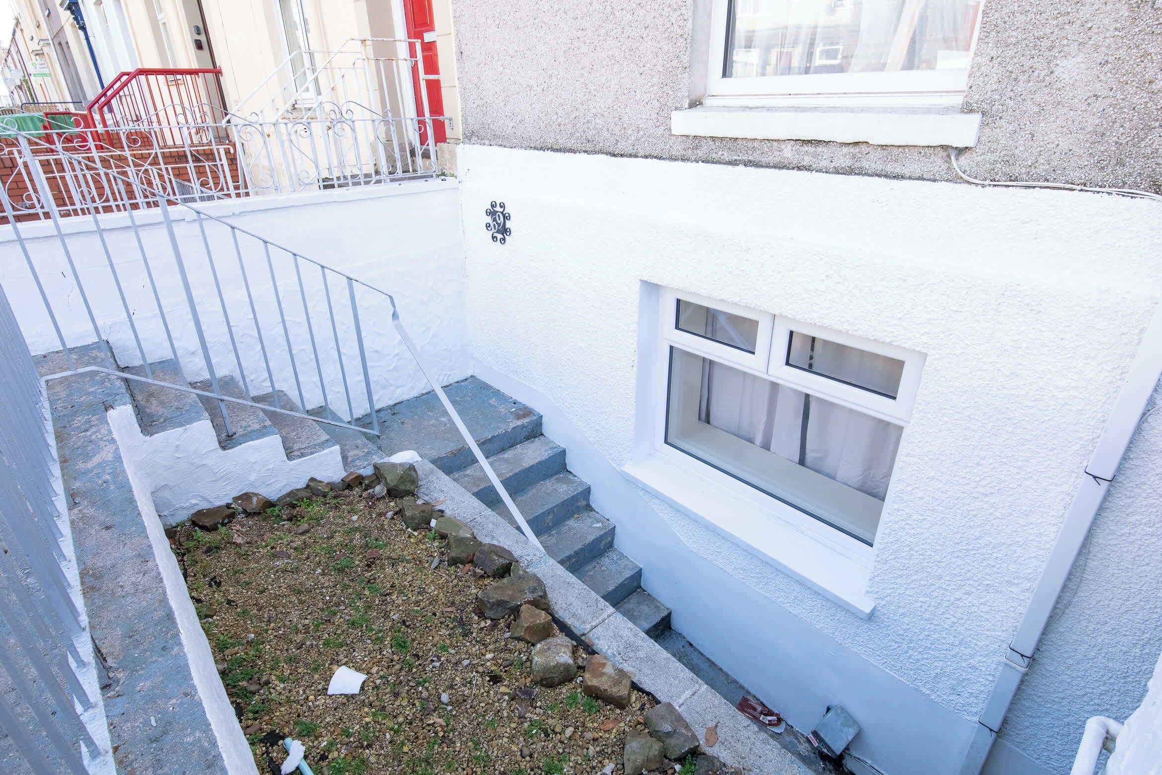 A white building with a small window and a set of stairs leading to a door.