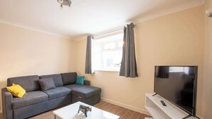 A living room with a grey sofa, a small white coffee table, a flat-screen TV on a white stand, and a window with grey curtains. - Host Stay Hanover Apartment (Swansea)