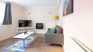 A modern living room with a flat-screen TV, a sofa with cushions, a coffee table, and a painting on the wall. - Host Stay Hanover Apartment (Swansea)