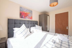 A hotel room with a large bed, a grey upholstered headboard, a wooden wardrobe, and a wooden door. - Host Stay Hanover Apartment (Swansea)