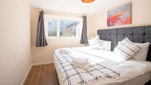 A bedroom with a large bed, grey headboard, and a window with curtains. - Host Stay Hanover Apartment (Swansea)