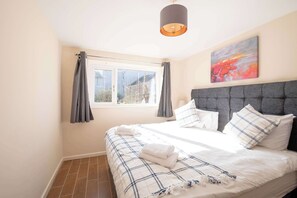 Camera da letto con un letto grande, testiera grigia e una finestra con tende.