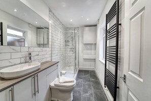 Ein modernes Badezimmer mit Marmorwaschbecken, weißer Toilette und einer Duschkabine aus Glas.