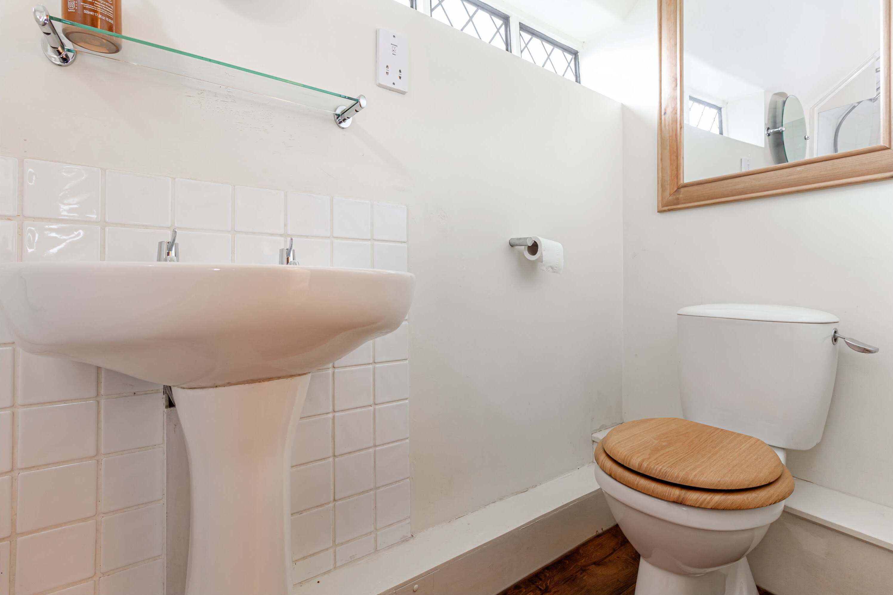 A bathroom with a white sink, a toilet with a wooden seat, and a mirror above the toilet.