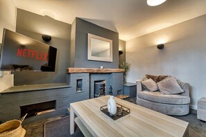 Un salon moderne avec une cheminée, un téléviseur fixé au mur diffusant du contenu « NETFLIX », un canapé et une table basse.