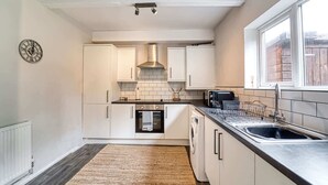 A compact kitchen with white cabinets, a stainless steel range hood, a built-in oven, a dishwasher, and a window providing natural light. - Host Stay Birches Barn (Wolverhampton)