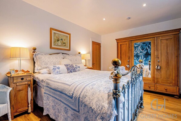 A bedroom with a large bed, wooden wardrobe, and a nightstand with a lamp. - Host Stay Little Highlands (Tenbury Wells)