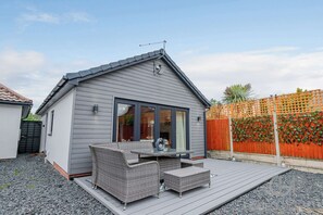 A small house with a deck, wicker furniture, and a window overlooking a garden. - Host Stay Little Highlands (Tenbury Wells)