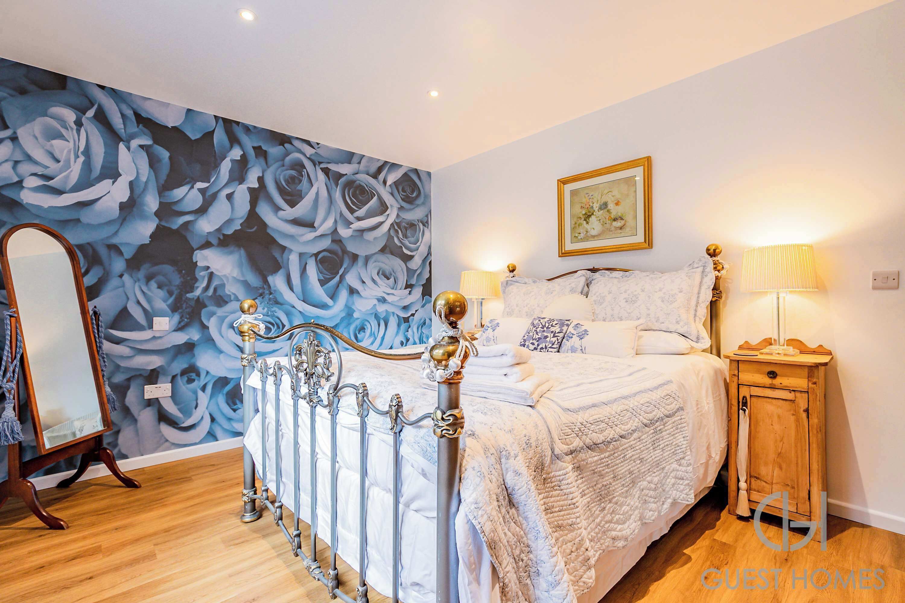 A bedroom with a bed, a nightstand, a mirror, and a floral wall mural.