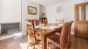 Une salle à manger avec une table en bois dressée pour quatre personnes, des chaises à rayures, un miroir, une horloge et un radiateur.