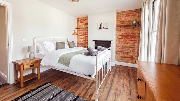 Une chambre avec un lit blanc, une table de chevet en bois et un mur décoratif en briques.
