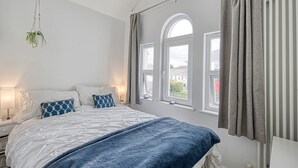 Une chambre à coucher avec un lit, des tables de chevet, une plante suspendue et une vue par la fenêtre.