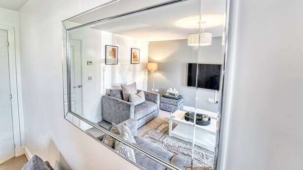 A modern living room with a large mirror, grey sofas, a coffee table, and a TV mounted on the wall. - Host Stay Walkers Lane House (Worcester)