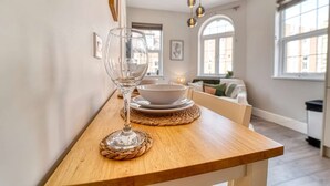 Una mesa de comedor con una copa de vino de vidrio transparente, un bol y posavasos. La habitación tiene una mesa de madera, paredes blancas y una ventana con luz natural.