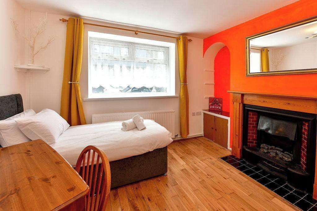A bedroom with a bed, a wooden table, a chair, a fireplace, and a window with curtains.