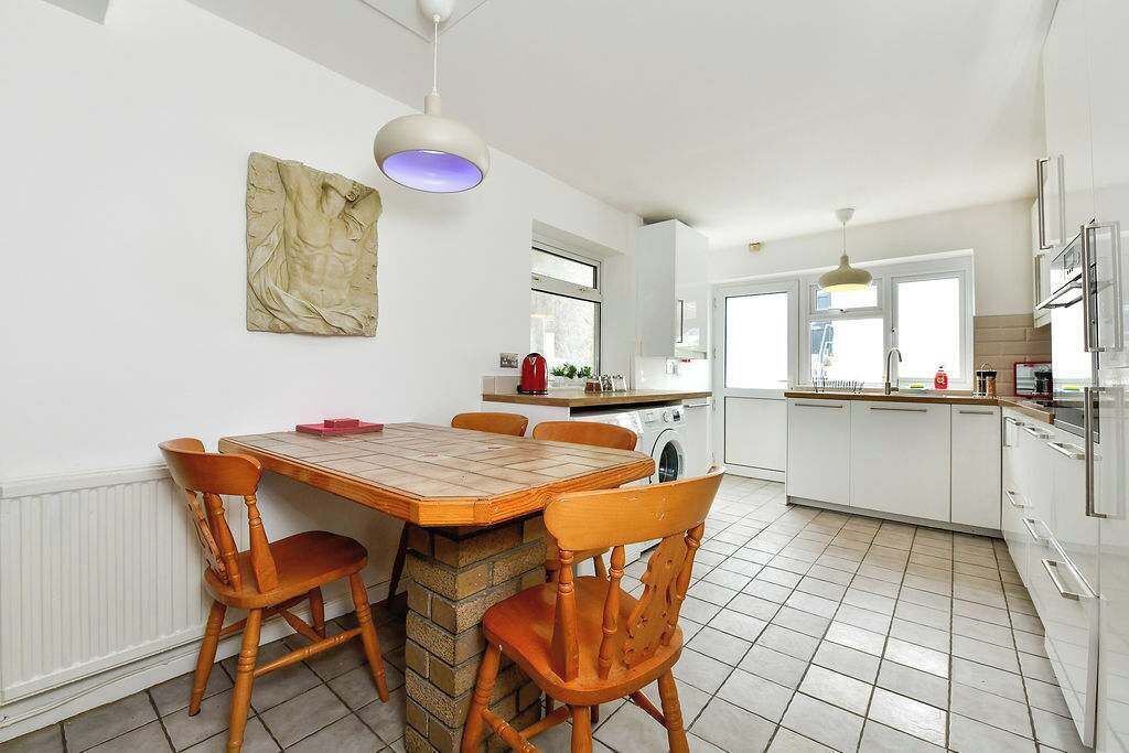 A modern kitchen with white cabinets, a wooden dining table, and a pendant light.