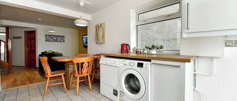 Eine kompakte Küche mit Waschmaschine, ein Essbereich mit Holzstühlen und ein kleines Fenster mit Ausblick.