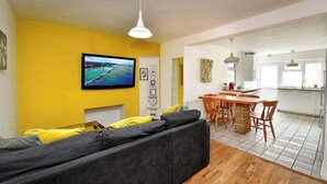 Uma sala de estar moderna com uma televisão grande, um sofá e uma área de jantar com mobiliário de madeira.