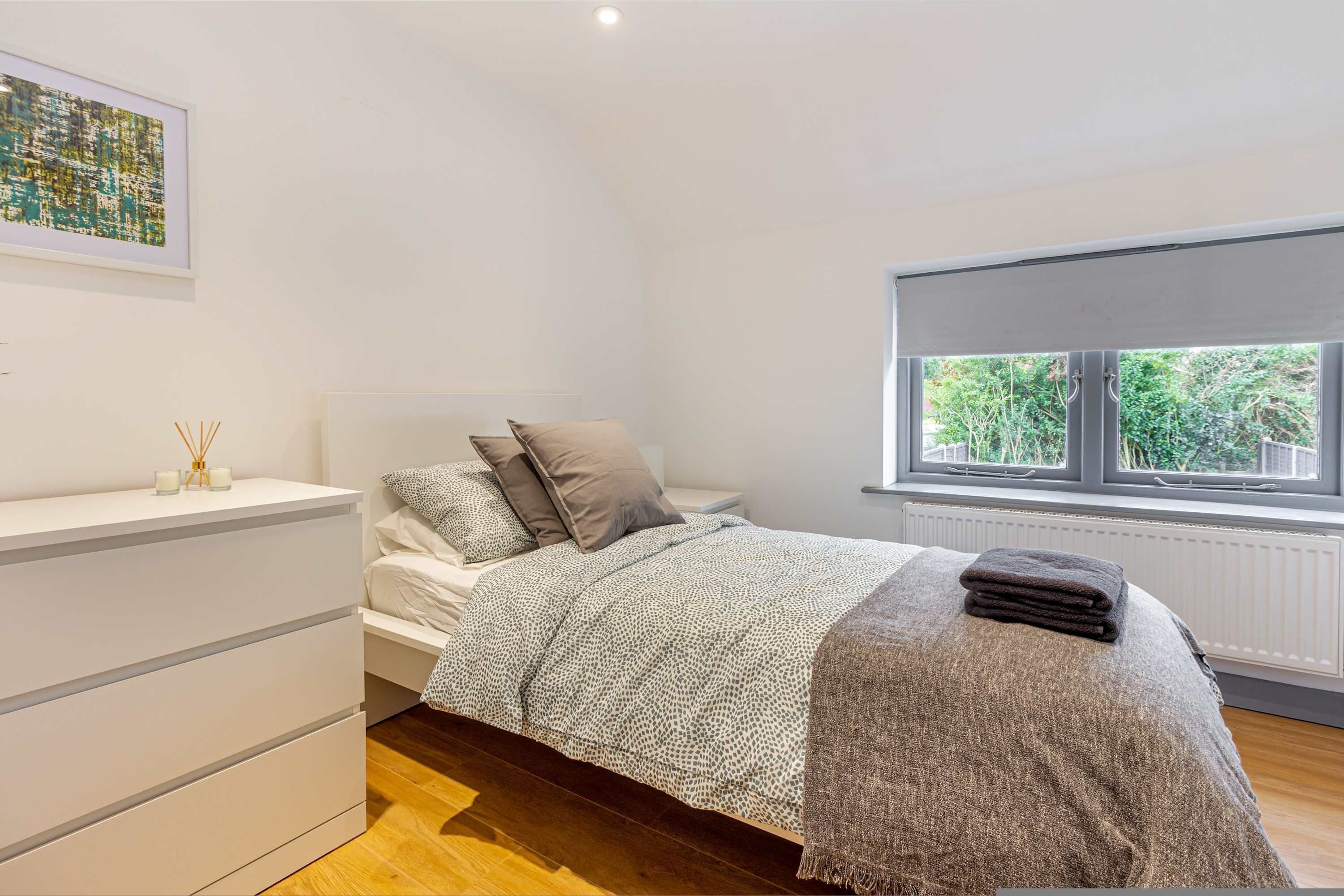 A bedroom with a bed, a bedside table, a window with a view of greenery, and a radiator.