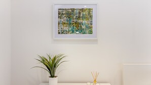A framed abstract painting, a potted plant, and two candles on a white table. - Host Stay Bridge Street Residence (Leominster)
