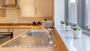 A modern kitchen with a stainless steel sink, wooden countertop, and potted cacti on the windowsill. - Host Stay Bridge Street Residence (Leominster)