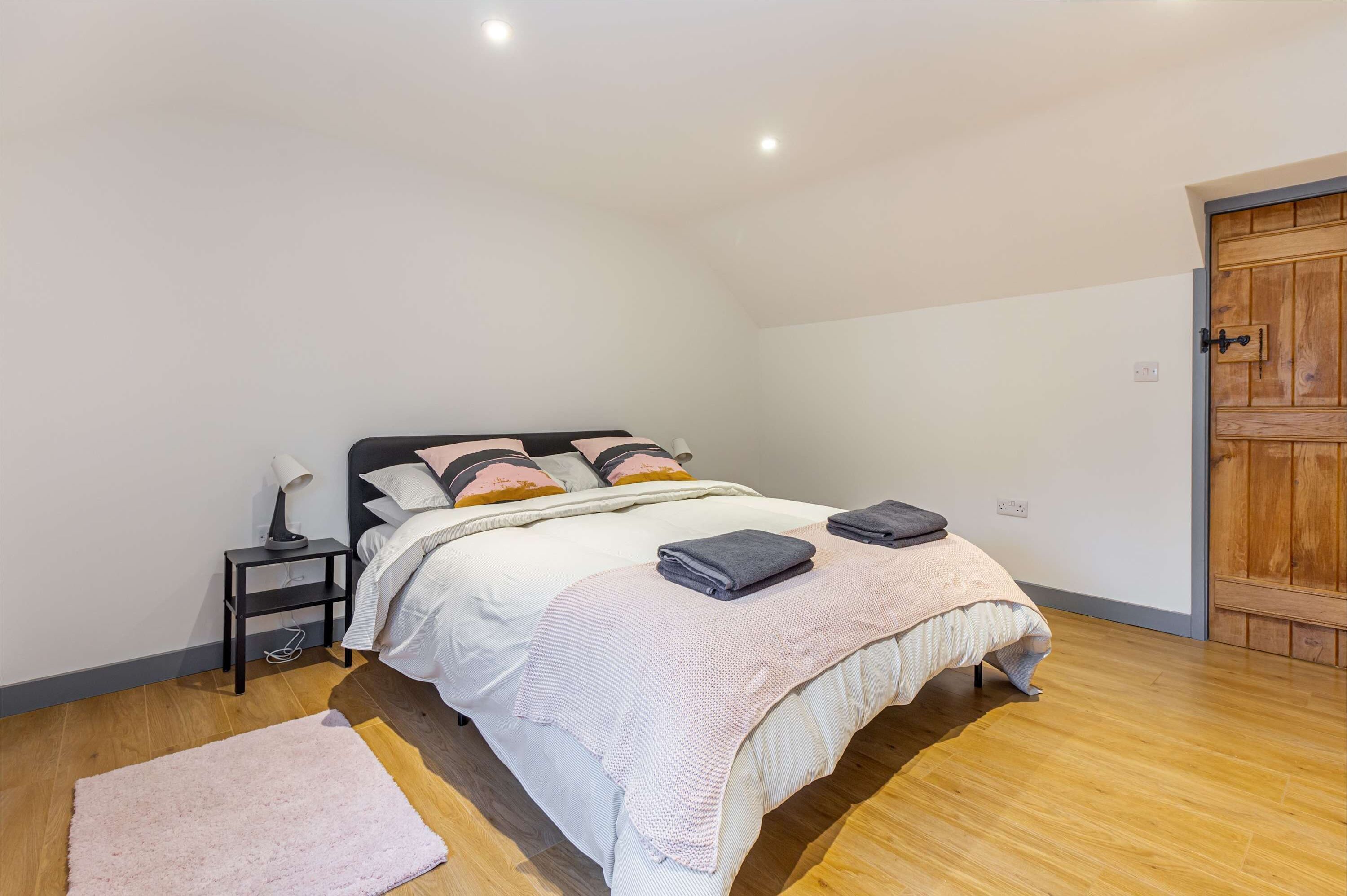 Un dormitorio con cama, mesita de noche, lámpara y una puerta de madera.