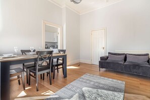 Een eethoek met een tafel voor vier personen, een grijze bank en een kamerbreed tapijt met patroon.