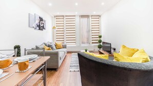Ein modernes Wohnzimmer mit einem grauen Sofa, einem schwarzen Sessel und einem Esstisch, gedeckt mit gelben Tassen.
