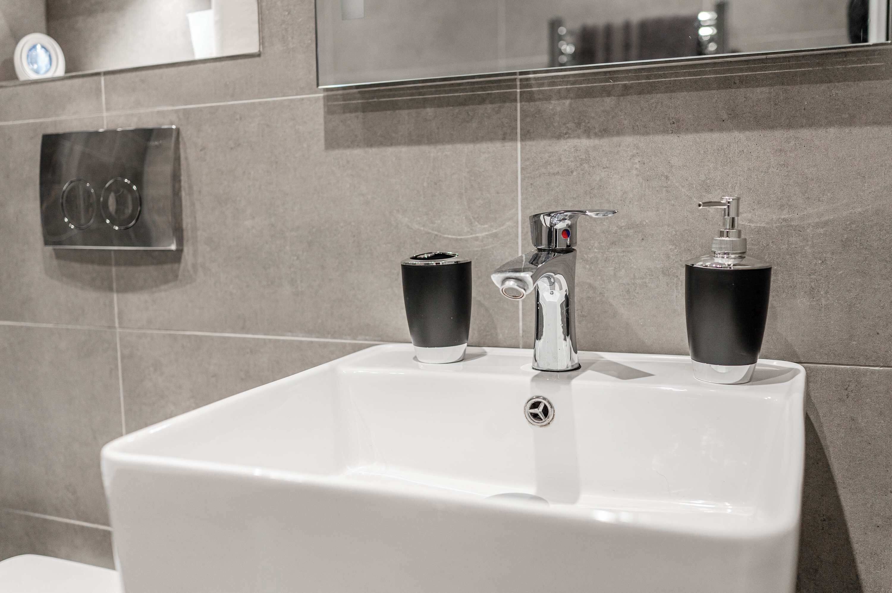 A modern bathroom with a white sink, two black soap dispensers, and a chrome faucet.