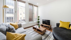 Ein modernes Wohnzimmer mit Sofa, Couchtisch, Fernseher und großen Fenstern.