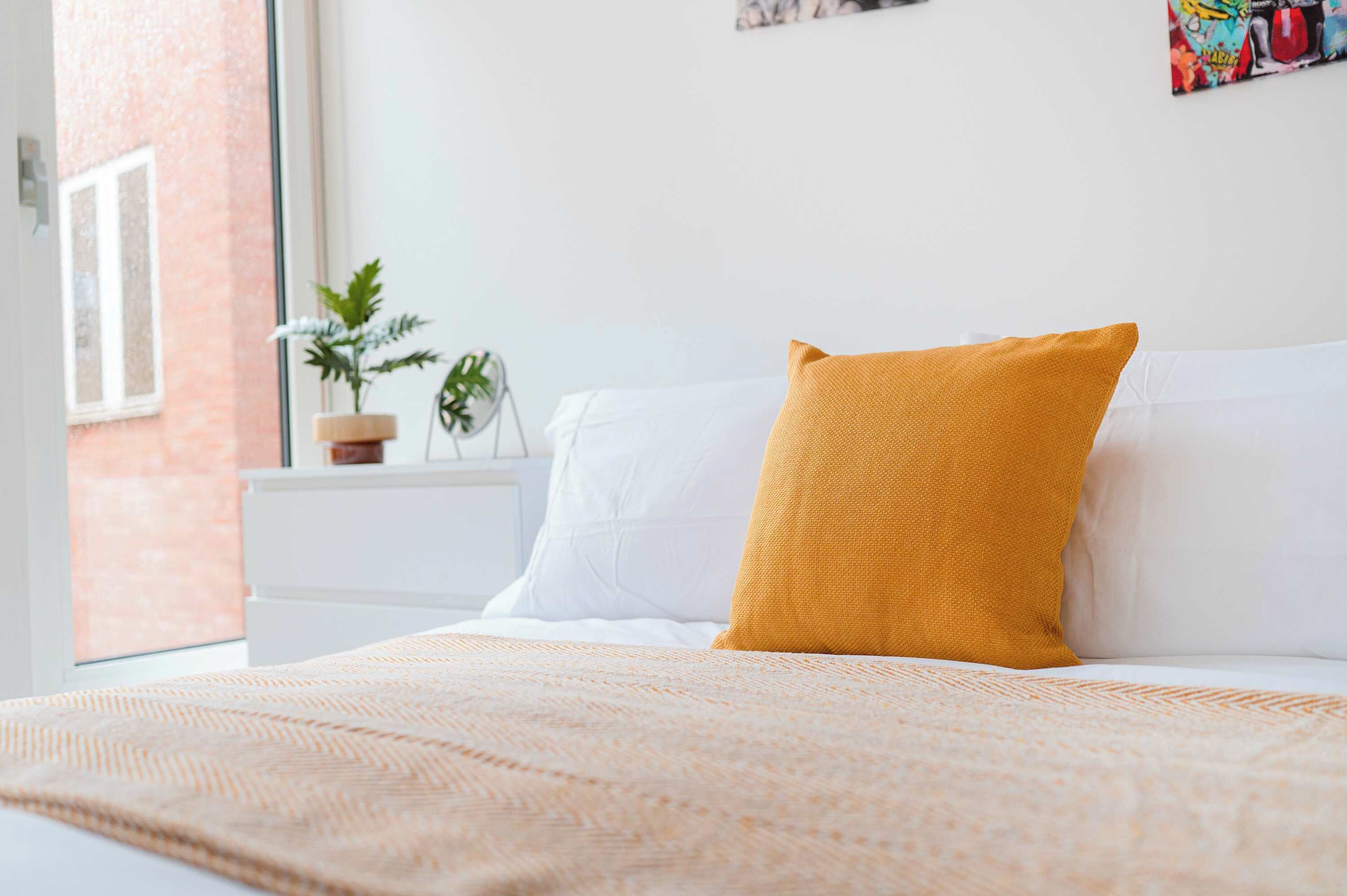 A neatly made bed with a white comforter and a mustard-colored pillow.