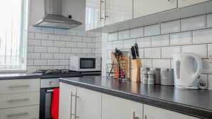Et moderne køkken med hvide skabe, et rustfrit stål emfang, en mikrobølgeovn og en elkedel på disken.
