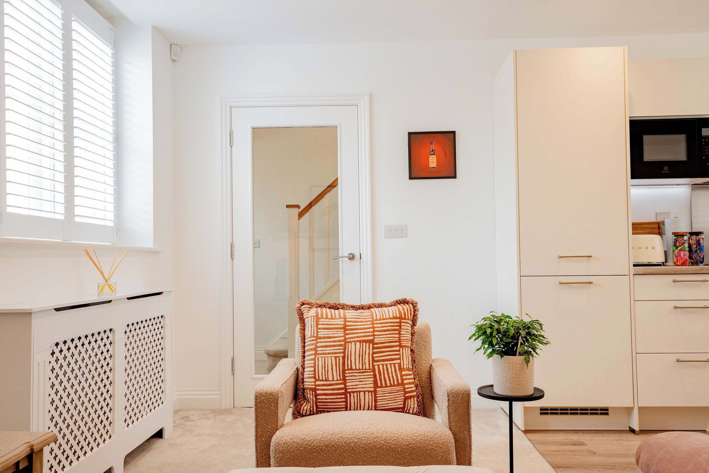 A compact living space with a kitchenette, a seating area with a patterned cushion, and a potted plant.