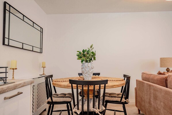 A dining area with a round wooden table, black chairs, and a vase with green plants. - Host Stay The Old School House (Worcester)