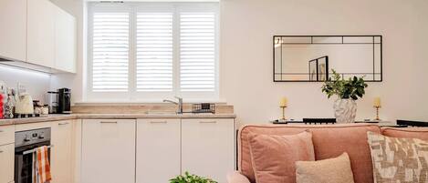 A modern kitchen with white cabinets, a built-in oven, and a window with blinds.