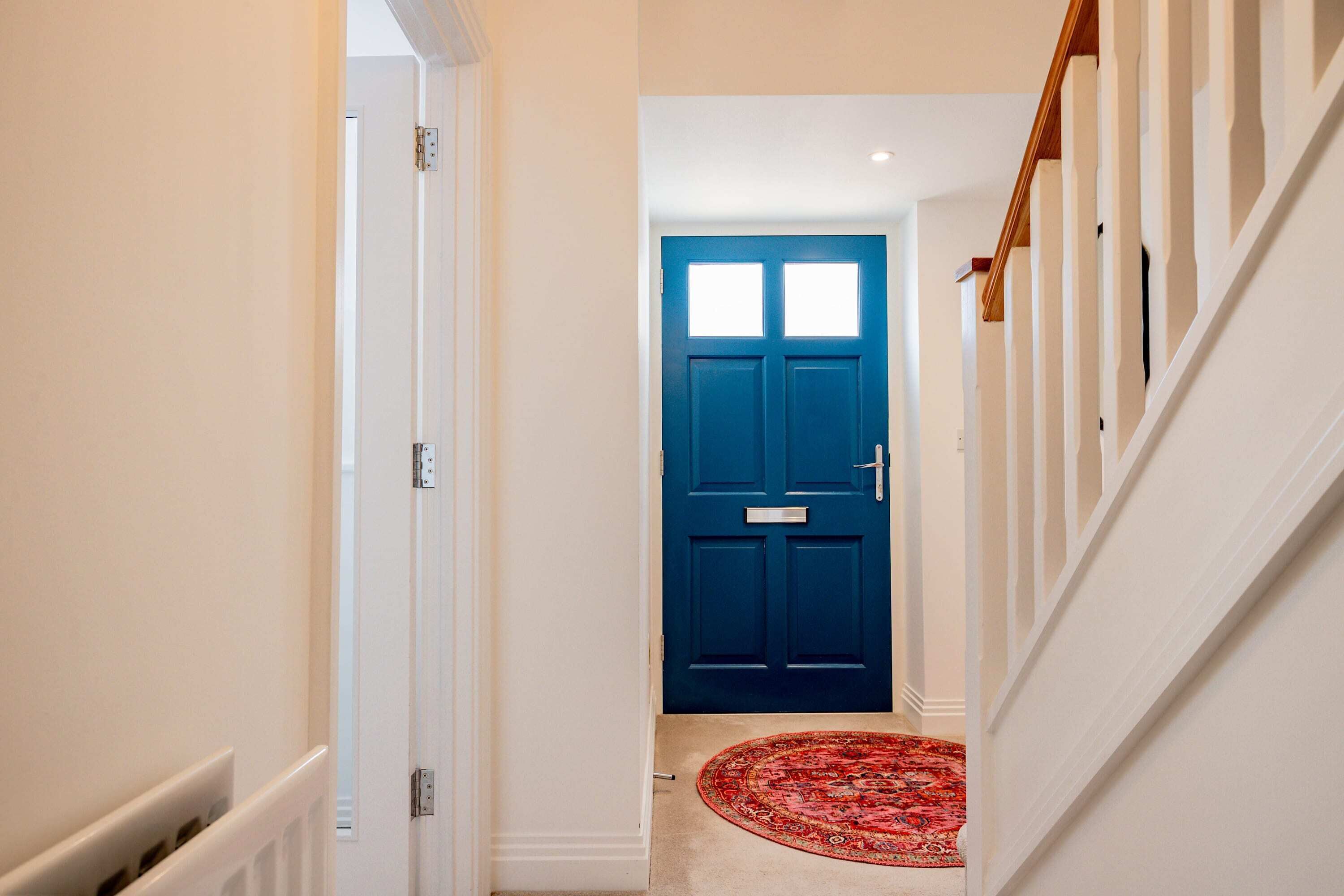 A hallway with a blue door, white walls, and a red patterned rug.