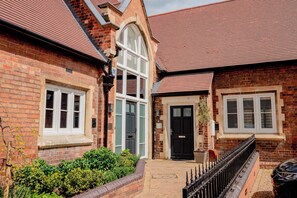 A brick building with a red-tiled roof, a central arched window, and a black door. - Host Stay The Old School House (Worcester)