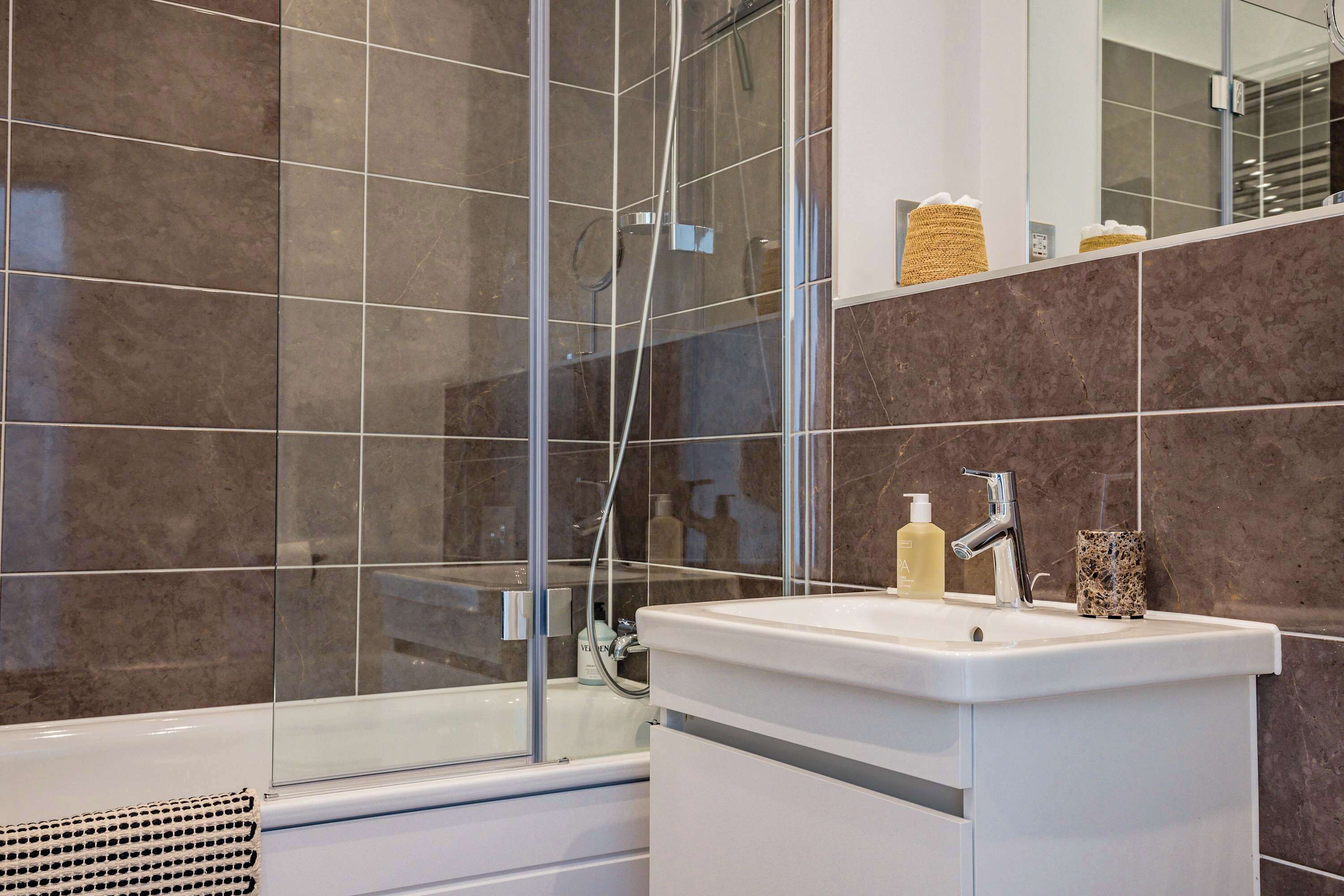 A modern bathroom with a glass shower enclosure, a white sink with a mirror, and toiletries on the countertop.