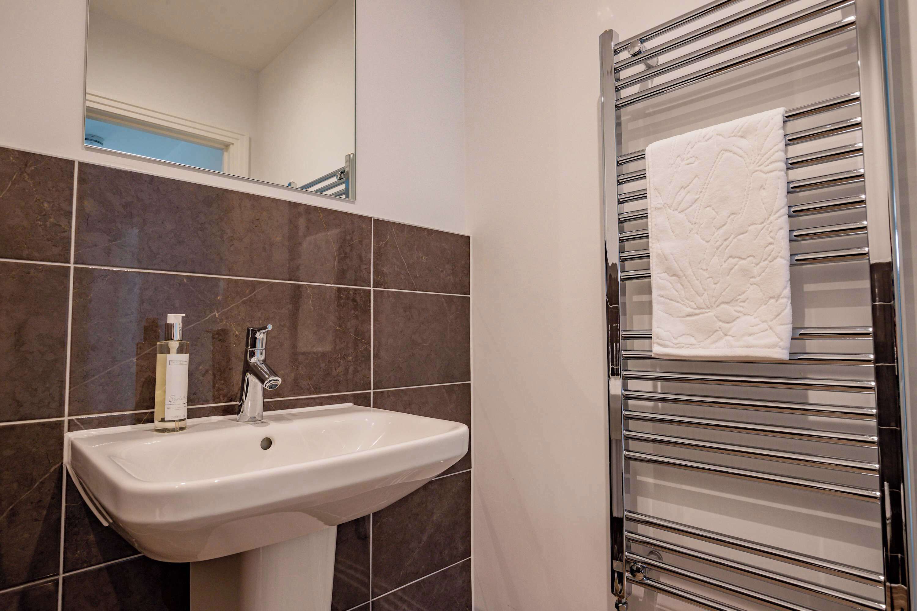 A bathroom with a white sink, a mirror, and a towel rack with a folded towel.