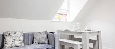 A modern loft bedroom with a gray sofa, a white dining table, and a skylight.
