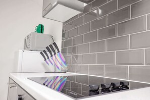 Modernilla designilla varustettu keittiö, jossa on lasinen liesitaso, valkoinen kodinkone ja laatoitettu välitila.