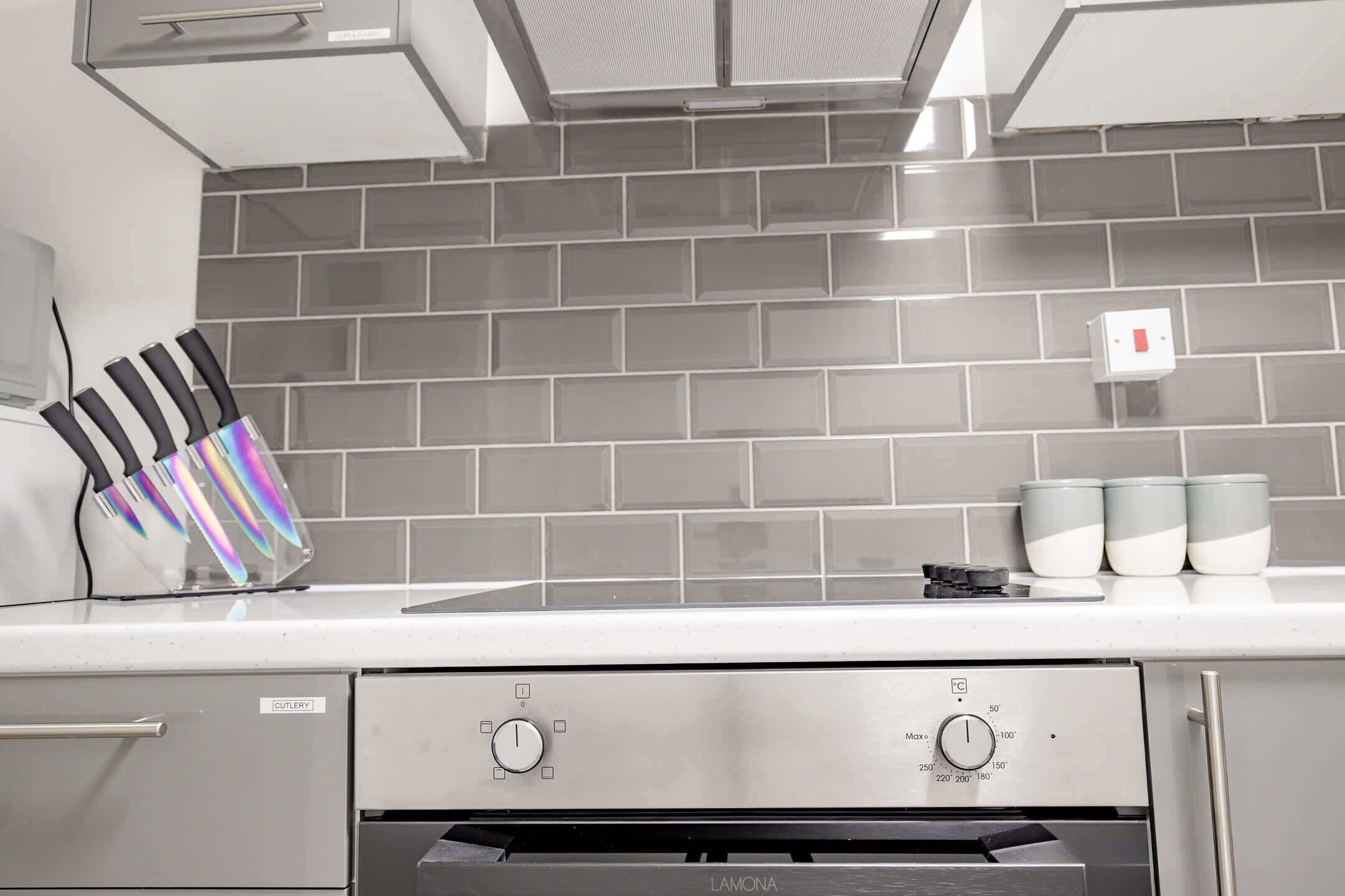 Una cucina con una cappa in acciaio inossidabile, forno integrato e backsplash in piastrelle grigie.