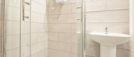 A modern bathroom with a glass shower enclosure, a pedestal sink, and beige tiled walls.