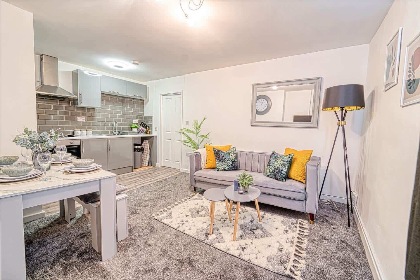 A modern living room with a grey sofa, coffee table, and a dining area with a white table and chairs.